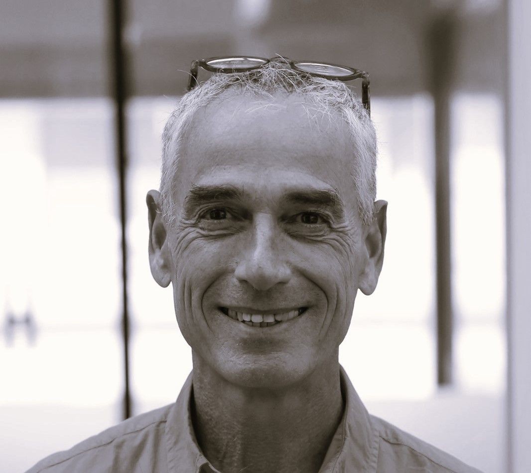 A person wearing glasses on their head with a blurry background, dressed in a collared shirt.